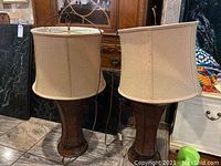 Pair of table lamps with beige fabric shades and wooden bases, front view.