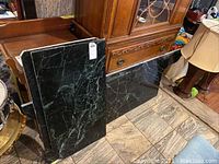Three green marble slabs stacked and leaning against furniture, showing polished veined marble surfaces.