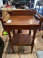 Wooden stand front view showing flat top with raised back and side handles, legs, and lower shelf. Visible nicks and scratches on surface.