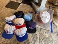 Seven Washington Bullets hats and signed basketball in clear display case on stone floor.