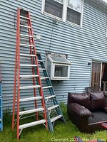 Red Louisville ladder and blue Werner ladder leaning against house siding on grass
