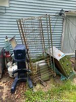 Garland grill, large blue floor mixer, and wire storage cart against exterior wall showing rust and outdoor wear.