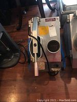 Top and side view showing slicing machine handle, housing, and power cord on wooden floor.