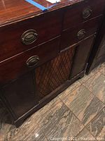Front upper view of vintage wooden stereo cabinet showing two drawers with brass handles and speaker grille with diamond lattice design.