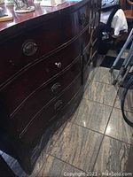 View of the front curved drawers of the vintage dresser showing multiple drawer fronts and missing hardware on at least one drawer.