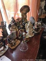 Group of Norman Rockwell style figurines, Christmas figurines, and the glass bell displayed on a wooden surface with natural light coming from behind.