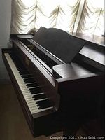 Left side view of the baby grand piano showing keyboard and open key cover with wood finish and some discoloration.