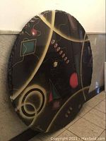 Full view of round abstract art table top leaning against wall, showing painted geometric shapes and lines
