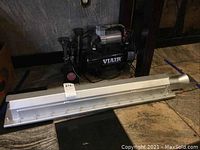 Photo showing the VIAIR air supply kit with triple horn mounted on the black compressor tank, electric motor visible on top, sitting on stone floor.