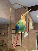 Full view of bird sculpture on metal trapeze perch hanging from ceiling