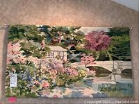 Full view of decorative tapestry showing house by river and bridge scene with vibrant flora.