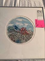 Framed circular artwork depicting a forest and mountain landscape scene, matted and behind glass frame.