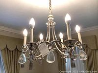 Full view of lit chandelier showing six arms with candle style LED bulbs and hanging glass pendants.