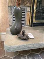 Both hourglass vase and leaf dish shown side by side on stone surface in front of fireplace