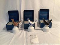 Three Royal Worcester porcelain birds on white stands with their original blue boxes behind them.