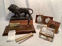 Seven vintage desk items including a metal lion sculpture on a wooden base, pen holder with calendar, Cross pen with sheath, brass and glass trinket box, and barometer.