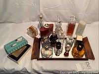 Front view showing full collection of glass perfume bottles on mirrored wooden tray, plus cigarette case compact and blue and white box to left.