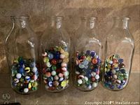 Four clear glass quart milk bottles filled with colorful glass marbles on a shelf.