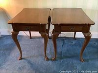 Two matching wooden porringer style end tables side by side on blue carpet, showing overall shape with Cabriole legs and scalloped tops.
