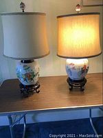 Frontal view of both lamps on table showing porcelain jars, shades, and stands