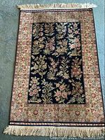 Full view of rectangular rug on light carpet floor, showing navy field with floral motifs, cream border and fringe at top and bottom.