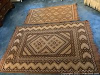 Two wool rugs side by side on blue carpet, showing overall size difference