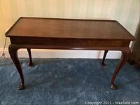 Full view of the Queen Anne style console table showing attached tray top, cabriole legs, and claw-and-ball feet resting on blue carpet.