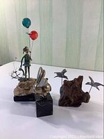 Overall view of the three sculptures showing Balloon Girl with balloons, Brass Bee replica on black marble stand, and unsigned bird sculpture on wooden base.