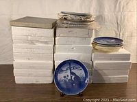 Stacked boxes each labeled with a year, and a single Christmas plate displayed in front showing a cat and snowy window scene in blue and white.