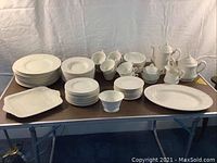 Full set displayed on folding table showing all plates, bowls, cups and serveware.