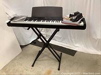 Full view of Yamaha P-80 electric piano on black X-style folding stand with books/manuals and power adapter on top of keyboard.
