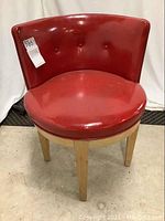 Front angled view showing red vinyl upholstery with button tufting on the backrest and round seat, wooden legs visible.