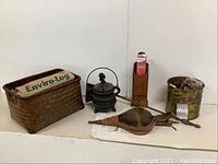 Wide shot showing woven basket with 3 Enviro-Logs, brass pot, brass shovel, turtle-back bellows, wooden match holder with matches, and cast iron fire pot placed on plain white background.