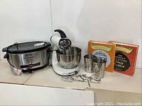 Wide shot showing the Sunbeam stand mixer with bowl and attachments, Kitchenaid crockpot, measuring cups, and two America's Test Kitchen cookbooks.