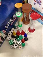 Photo showing 4 different hourglass timers (orange, green, wooden, red), white and green dice, and colored game pieces