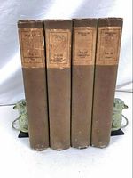 Four hardcover books with brown dust jackets standing upright and showing wear on jackets. Titles and volume numbers visible on paper labels attached to spines.
