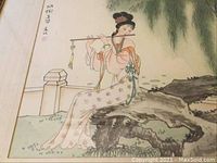 Close-up photo of the watercolor painting depicting a seated woman playing flute, showing detail of brushwork and calligraphy.