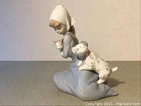 Front and side view of porcelain figurine showing girl in dress with puppy climbing on back and kitten in arms.