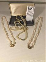 Three vintage pearl necklaces displayed with clasps visible, showing knotted strands and clasp details.
