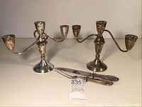 Two three-arm sterling silver candleholders showing some tarnishing and patina typical for their age, standing with weighted bases.