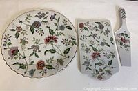 Overall view of round cake plate, rectangular cheese plate, and cheese server showing floral patterns and gold trim on white background