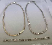 Photo of two sterling silver necklaces (flat and braided) and one linked bracelet laid out on a light surface.