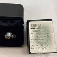 Ring in black jewelry box next to original box showing label with ring details including size 7.5 and aquamarine stone.