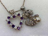 Close-up of the heart and elephant charms on silver chain, showing purple amethyst and clear stones on heart, rhinestones and pearl on elephant.