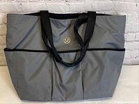 Front view of gray Lululemon tote bag with black handles and Lululemon logo on front