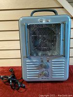 Front view of Comfort Zone metal space heater showing handle, mesh grill and control panel with power and caution indicators and control knobs.