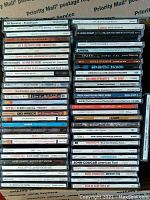 Photo of 59 compact discs stacked in multiple rows in a box, showing various album spine titles and artists.