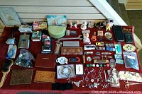 Top overview photo of assorted small items laid out on red cloth including jewelry, collectibles, boxes, personal care items, and household products.