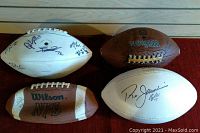 All four footballs arranged on a surface showing visible autographs on white and brown footballs.