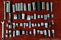 Photo showing a wide assortment of metal sockets, extensions, a universal joint, and an open-end wrench laid out on a surface.